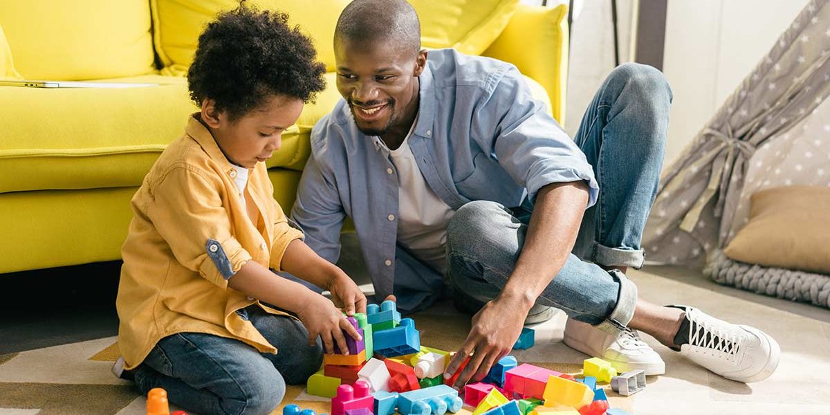 Vater und Sohn sitzen vor gelbem Sofa auf dem Boden und spielen mit Bauklötzen - Scheidungsimmobilie