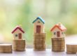 Drei Modellhäuschen stehen auf Stapeln von Münzen - Immobilienfinanzierung