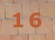 Orange Zahl 16 auf gemauerter Häuserwand.