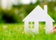 Hand hold house against green field; Immobilienkauf