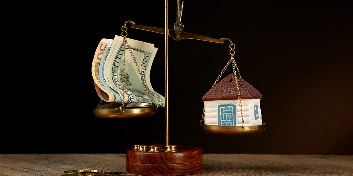 Scale with money and model of house on dark background; Wertermittlung