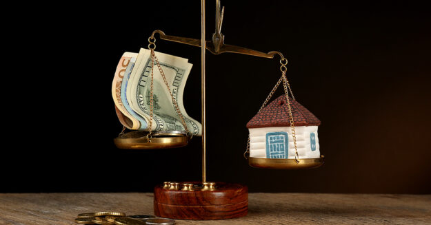 Scale with money and model of house on dark background; Wertermittlung