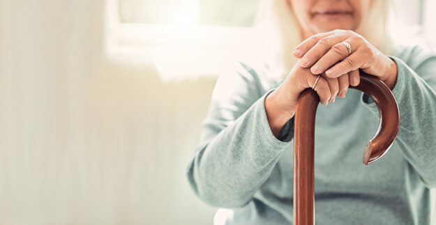 Growing old is inevitable, but growing up is optional. elderly woman resting her hands on her walking stick while relaxing at home; Wohnen im Alter