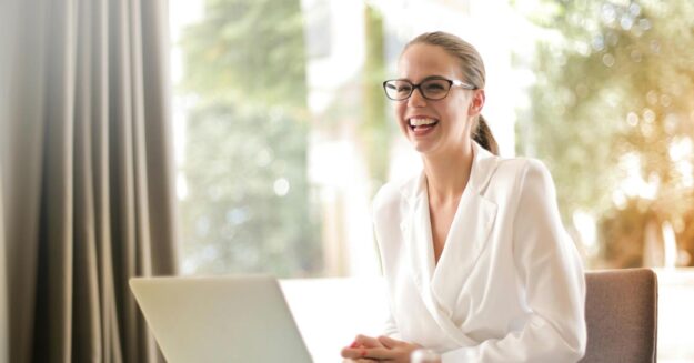 Eine Frau sitzt lachend an ihrem Laptop und freut sich über die gute Online-Bewertung ihrer Immobilie | Immobilienbewertung