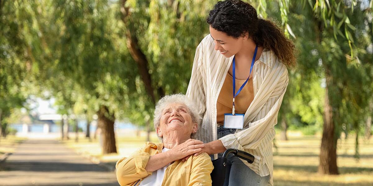 Eine Seniorin in ihrem Rollstuhl und ihre Pflegerin