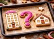 Weihnachtliche Plätzchen in Form eines Mehrfamilienhauses, eines Einfamilienhauses und eines Fragezeichens auf einem Backblech – Symbolbild für die Entscheidung „Miete oder Kauf“ und Wohnfragen 2026. | Immobilienkauf